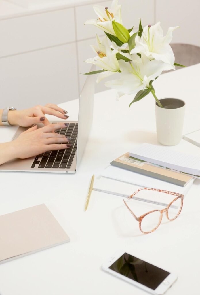 A serene workspace featuring a laptop, flowers, and office supplies on a white desk.