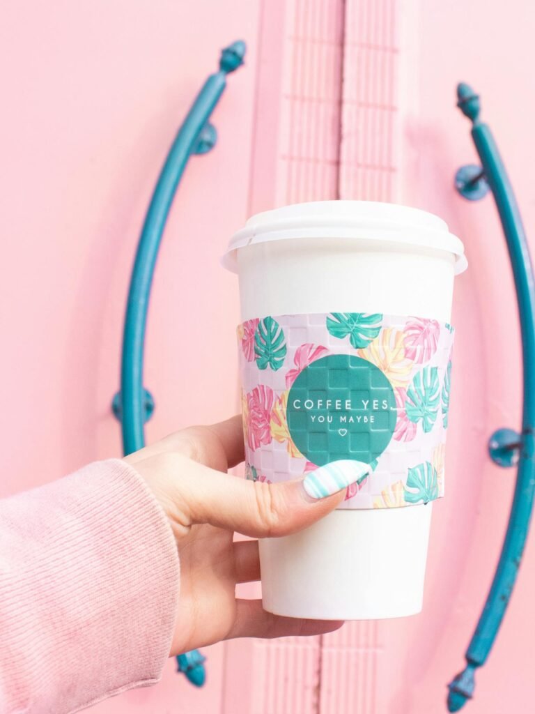 A vibrant coffee cup with floral design held in front of a pink door adds a pop of color.