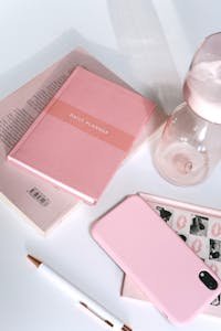 Modern pink-themed desk layout featuring a planner, phone, pen, and accessories.