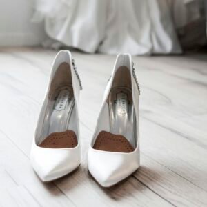Stylish white bridal shoes positioned in front of a flowing wedding dress indoors.